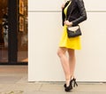 A super fashionable long-legged girl with in a short yellow dress, black high heels with a large black handbag makes shopping near