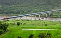 Super fast train crosses long viaduct on river at scenic location of green fields on Konkan Railway route Royalty Free Stock Photo