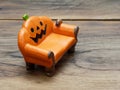 Super or giant worm crawling on orange miniature ceramic pumpkin couch or sofa over dark wooden surface