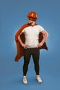 Super hero engineer. Man wearing red helmet, mask and cape standing with his hands on hips. Isolated on faded denim blue Royalty Free Stock Photo