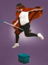 Super hero flying on mop. Funny man have fun with a bucket and a mop on grape purple background. Funny cleaning concept