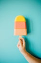 Super minimalistic hand grabbing a colorful foam ice cream in front of a pastel blue wall
