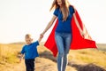 Super mom and her son walk forward holding hands. Cheerful family, a woman in a red raincoat as a superhero