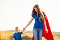Super mom and her son walk forward holding hands. Cheerful family, a woman in a red raincoat as a superhero