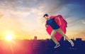 Man in superhero cape flying over sunset in city Royalty Free Stock Photo