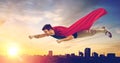 Man in superhero cape flying over sunset in city Royalty Free Stock Photo