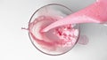 Super-slow motion of strawberry yogurt pouring into transparent glass in white background, top view