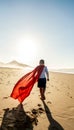 Superhero child walking on the sandy, sunset beach, wearing red mask and cape. Back view. Full length. Summer vacation concept Royalty Free Stock Photo