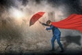 Superhero standing holding red umbrella protection,rain and storm,sky and black cloud,city background,with business,insurance, Royalty Free Stock Photo