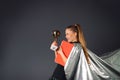 Superheroine, businesswoman with red folder and a champions cup in hands being satisfied of trophy on a gray background Royalty Free Stock Photo