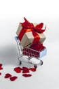 A supermarket cart filled to the brim with red confetti hearts and a gift box wrapped in kraft paper and tied with a red ribbon on Royalty Free Stock Photo