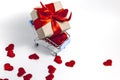 A supermarket cart filled to the brim with red hearts and a gift box wrapped in kraft paper and tied with a red ribbon on a white Royalty Free Stock Photo