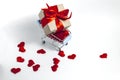 A supermarket cart filled to the brim with red hearts and a gift box wrapped in kraft paper and tied with a red ribbon on a white Royalty Free Stock Photo