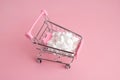 A supermarket cart filled to the brim with white candy hearts on a pink background. The concept of buying presents