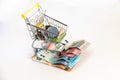 Supermarket shopping cart with essential goods and several euro banknotes on a white background.
