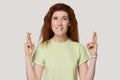 Superstitious millennial red-haired woman crossing fingers and biting lip portrait.