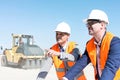Supervisor explaining plan to colleague at construction site against clear sky