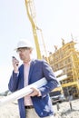 Supervisor using walkie-talkie while holding blueprints at construction site Royalty Free Stock Photo