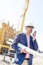 Supervisor using walkie-talkie while holding blueprints at construction site Royalty Free Stock Photo