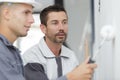 Supervisor watching apprentice painter use roller