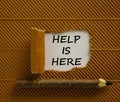 Support and help is here symbol. Words `help is here` appearing behind torn brown paper. Beautiful brown background. Wooden penc