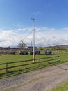 A supported Ships Mast with a carved wooden Fish on top, overlooks a field of Tractors and Boats next to a small Cottage. Royalty Free Stock Photo