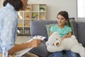 Cute little girl talking to child psychologist during therapy session in cozy modern office Royalty Free Stock Photo