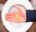 Suppository for constipation in the hand of an elderly person in the toilet against the background of the toilet bowl