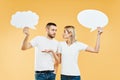 Suprised woman and man holding paper thought bubbles over yellow background