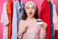 Suprised woman with opened mouth holds credit card. Lady wears pink sweater points aside at card. Glad female has money for Royalty Free Stock Photo