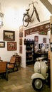 A room with a vintage interior is equipped with wooden chairs, Vespa motorbikes and old bicycles