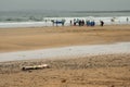 Surf board on a beach in focus. Group of surfers in wet suits out of focus in the background. Cloudy sky over the ocean. Royalty Free Stock Photo