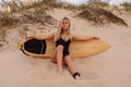 Surf girl in swimsuit sitting with surfboard on beach with warm sunset or sunrise tones Royalty Free Stock Photo