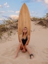 Surf girl in swimsuit sitting with surfboard on beach with warm sunset or sunrise tones Royalty Free Stock Photo