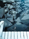 Surface of the lake with cracked ice. Black water with frozen parts. Wooden boards under snow.