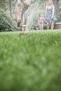 Surface level shot of father jumping through a sprinkler in the grass, mother and daughter watch in the background Royalty Free Stock Photo