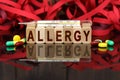 On the surface are visible pills, a thermometer, wooden dies and their reflections on which it is written - ALLERGY