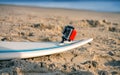 Surfboard with attached action camera lies on the sand