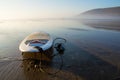 A surfboard on a beach reflected by the water on the sand. On a beautifully misty afternoon. Saunton, Devon, UK