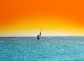 Surfer on blue sea under orange sky