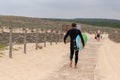 Surfer carrying surfboard going to the sea in black diving suits to surf walk to ocean in Lacanau France