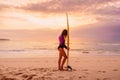 Surfer girl posing with surfboard on a beach at sunset