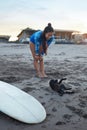 Surfer Girl. Surfing Woman Playing With Dog On Sandy Beach. Smiling Brunette In Blue Wetsuit. Royalty Free Stock Photo