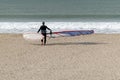 Surfer on a golden sand beach heading into the sea with his windsurf board Royalty Free Stock Photo