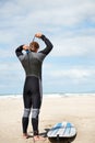 Surfer, man and getting ready with surfboard on beach with wetsuit, blue sky and dressing with mock up space. Rear view Royalty Free Stock Photo