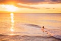 Surfer in ocean at bright sunset or sunrise. Winter surfing in sea