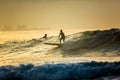 A surfer with a paddle rides on the crest of a large wave with foam at dawn