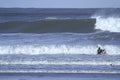 A surfer paddles on his surfboard towards a breaking approaching wave on a beach in Portugal Royalty Free Stock Photo