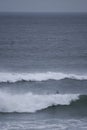 A surfer paddles on his surfboard towards a breaking approaching wave on a beach in Portugal Royalty Free Stock Photo