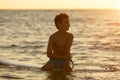 Surfer sitting on a surfboard at dawn - boy - in swimming shorts awaiting high waves on the beach